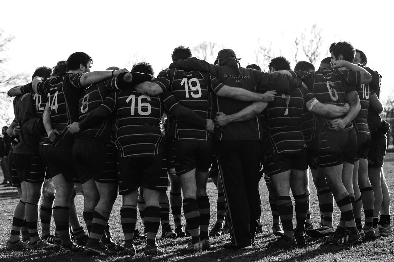 Sportteam im Mannschaftskreis (Huddle), Arme umeinander gelegt — Sinnbild für Zusammenhalt im Verein
